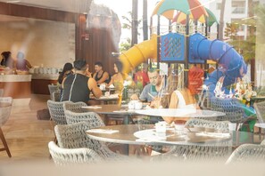 A restaurant with round tables and wicker chairs, a play structure outside, and a counter with staff. - Premium - GAV Hoteis e Resorts (Salinópolis)