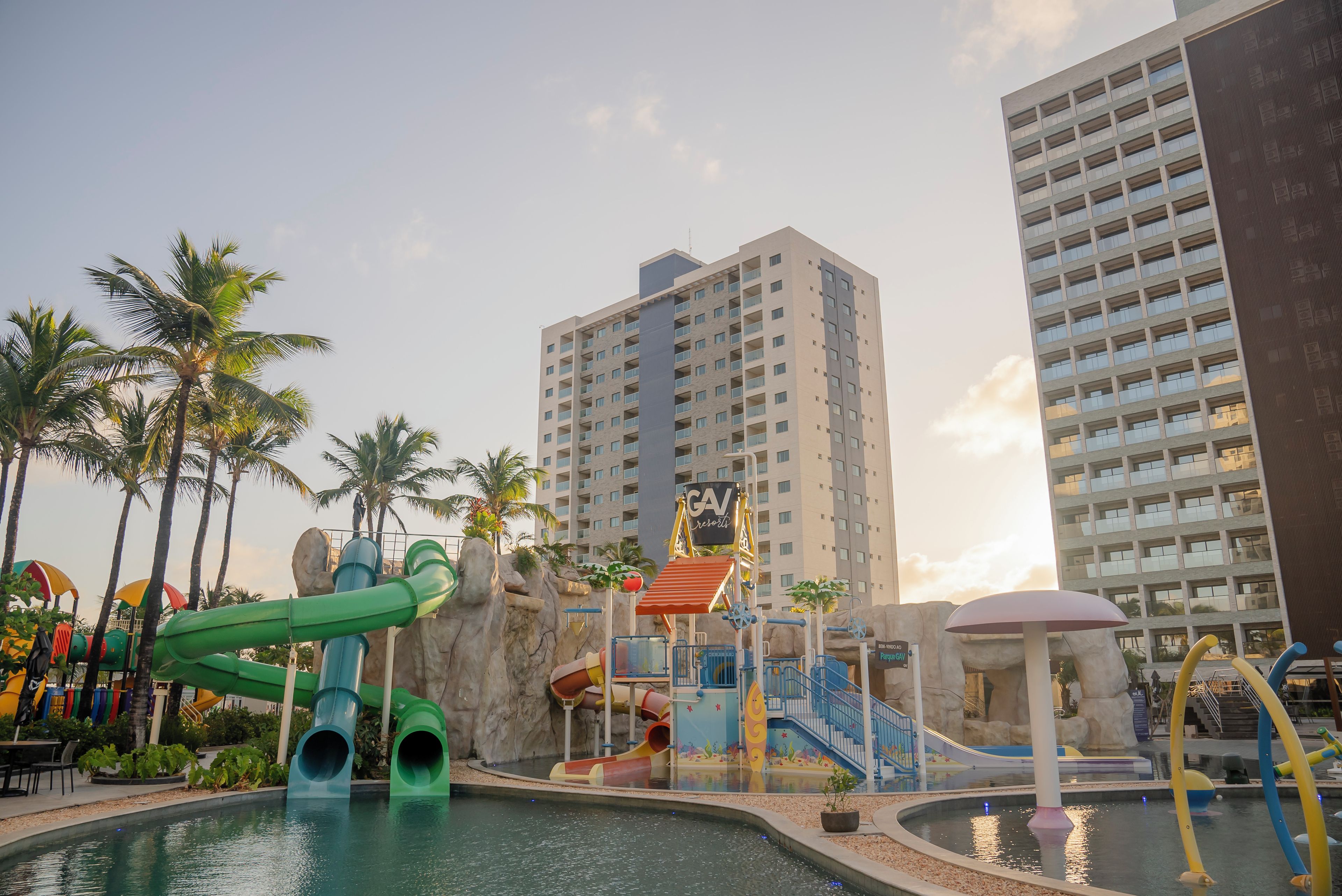 A water park with slides and a pool, surrounded by palm trees and tall buildings.