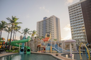 A water park with slides and a pool, surrounded by palm trees and tall buildings. - Premium - GAV Hoteis e Resorts (Salinópolis)