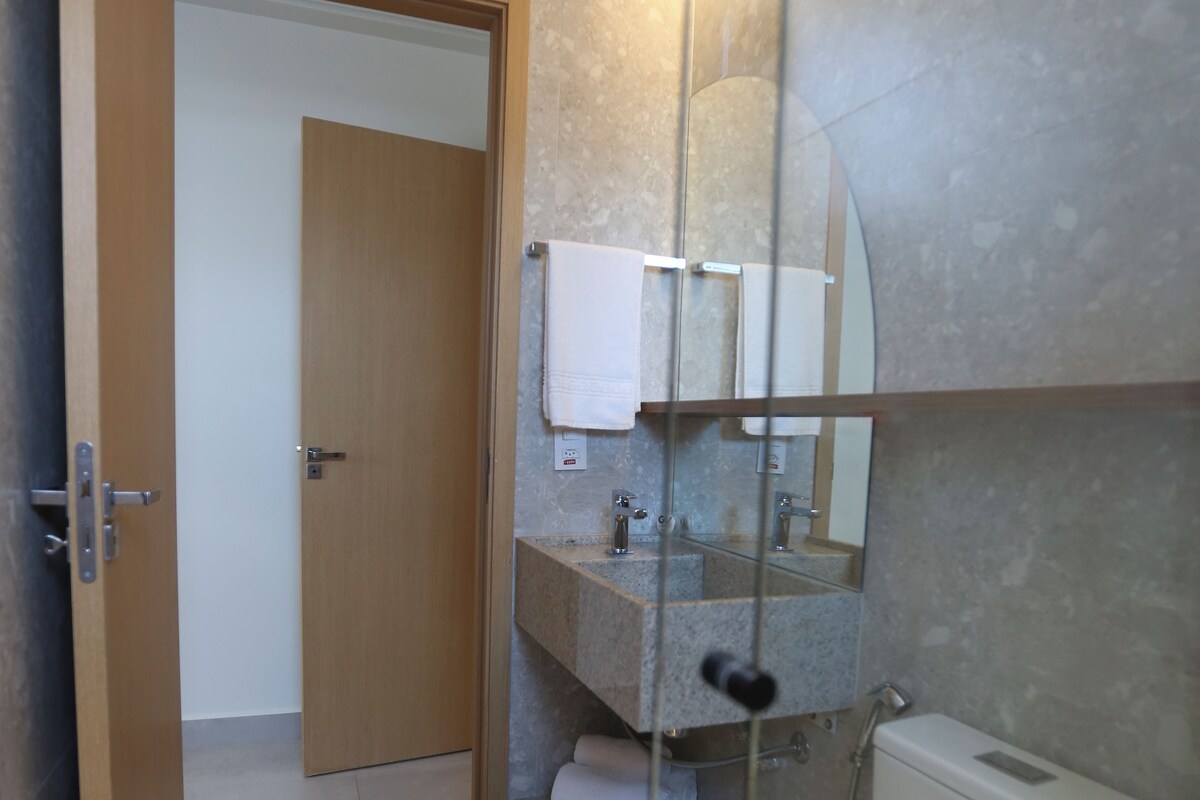 A bathroom with a toilet, sink, and mirror. There is a towel rack above the sink and a door leading to another room.