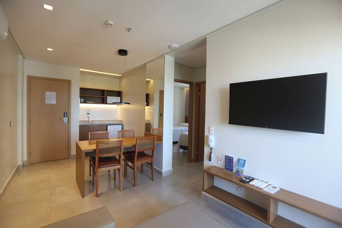 Ein modernes Hotelzimmer mit Essbereich, einem flachbildfernseher an der Wand und einer kleinen Ablage mit Informationsbroschüren.