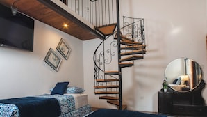 Un dormitorio con escalera de caracol, dos camas con ropa de cama estampada, un espejo grande y un televisor de pantalla plana montado en la pared.