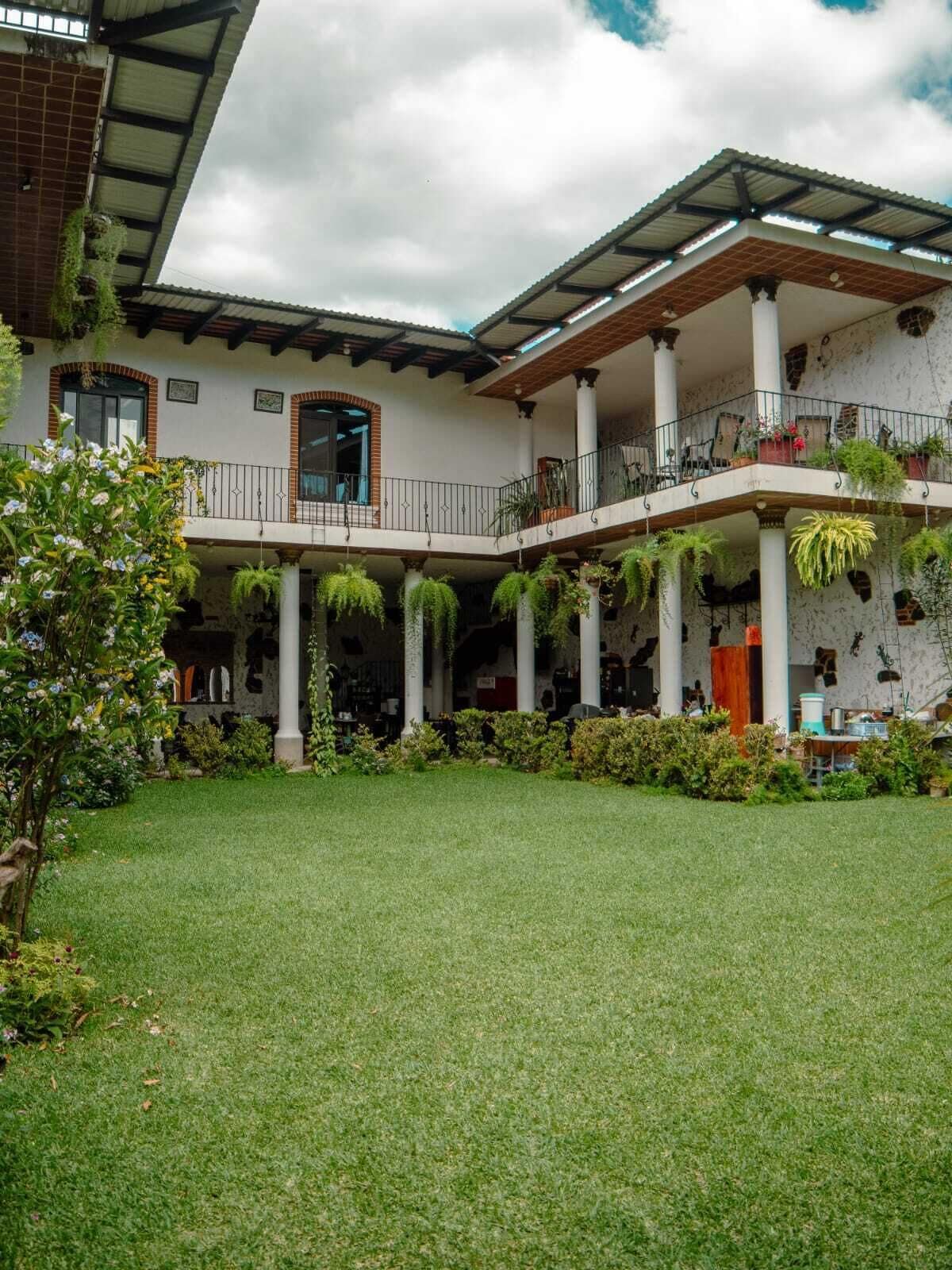 Un edificio de dos pisos con un patio cubierto, columnas y plantas colgantes.