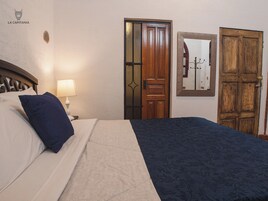 A hotel room with a bed, a nightstand with a lamp, a wooden door, and a mirror on the wall.