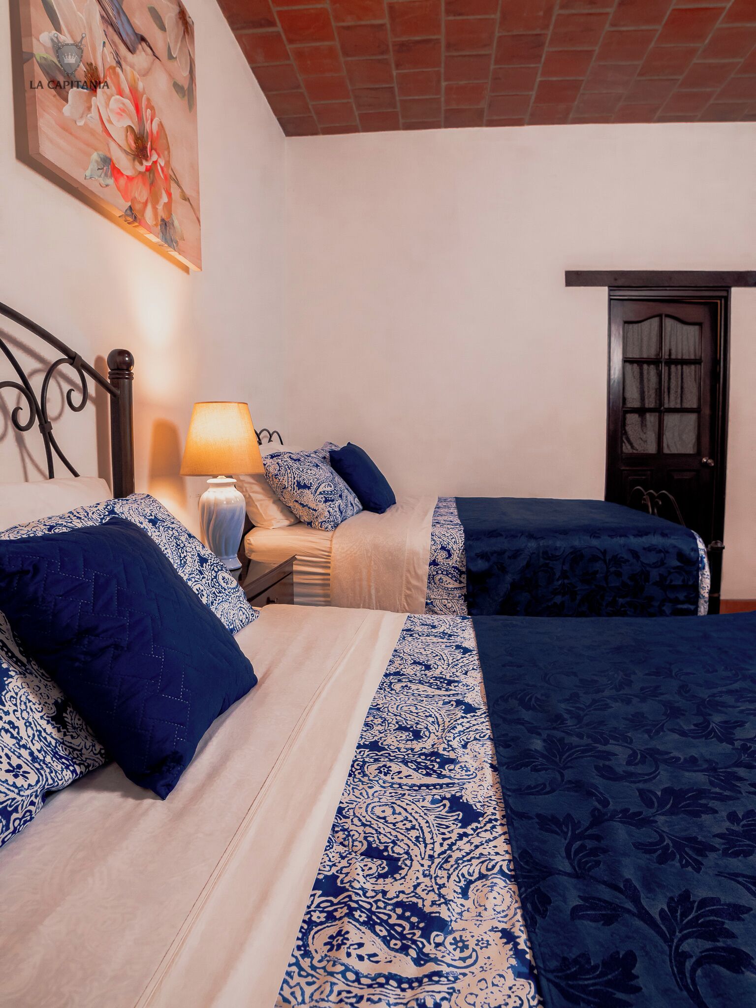 A bedroom with two beds, a nightstand, a lamp, and a door.