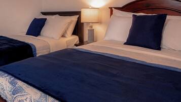 Una habitación de hotel con dos camas, una mesita de noche con lámpara y un cuadro en la pared.