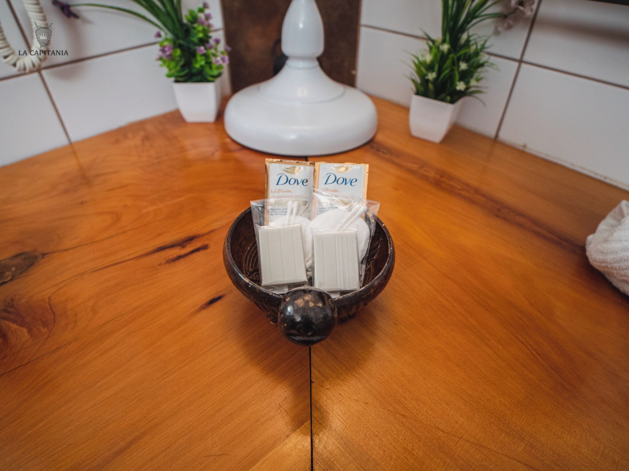Ein Holztisch mit einer schwarzen Schüssel, in der Taschentücher von Dove liegen, und eine weiße Lampe im Hintergrund.