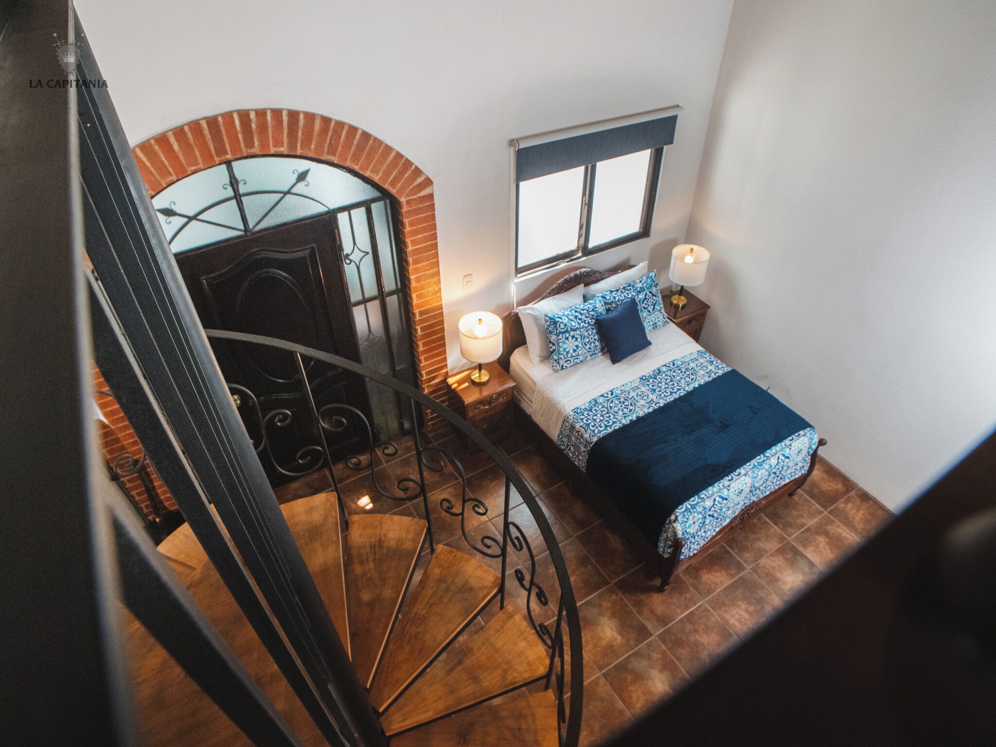 Un dormitorio con cama, ventana, mesita de noche y escalera.