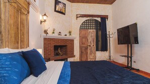 A bedroom with a bed, a fireplace, a TV stand, and a door with a window.
