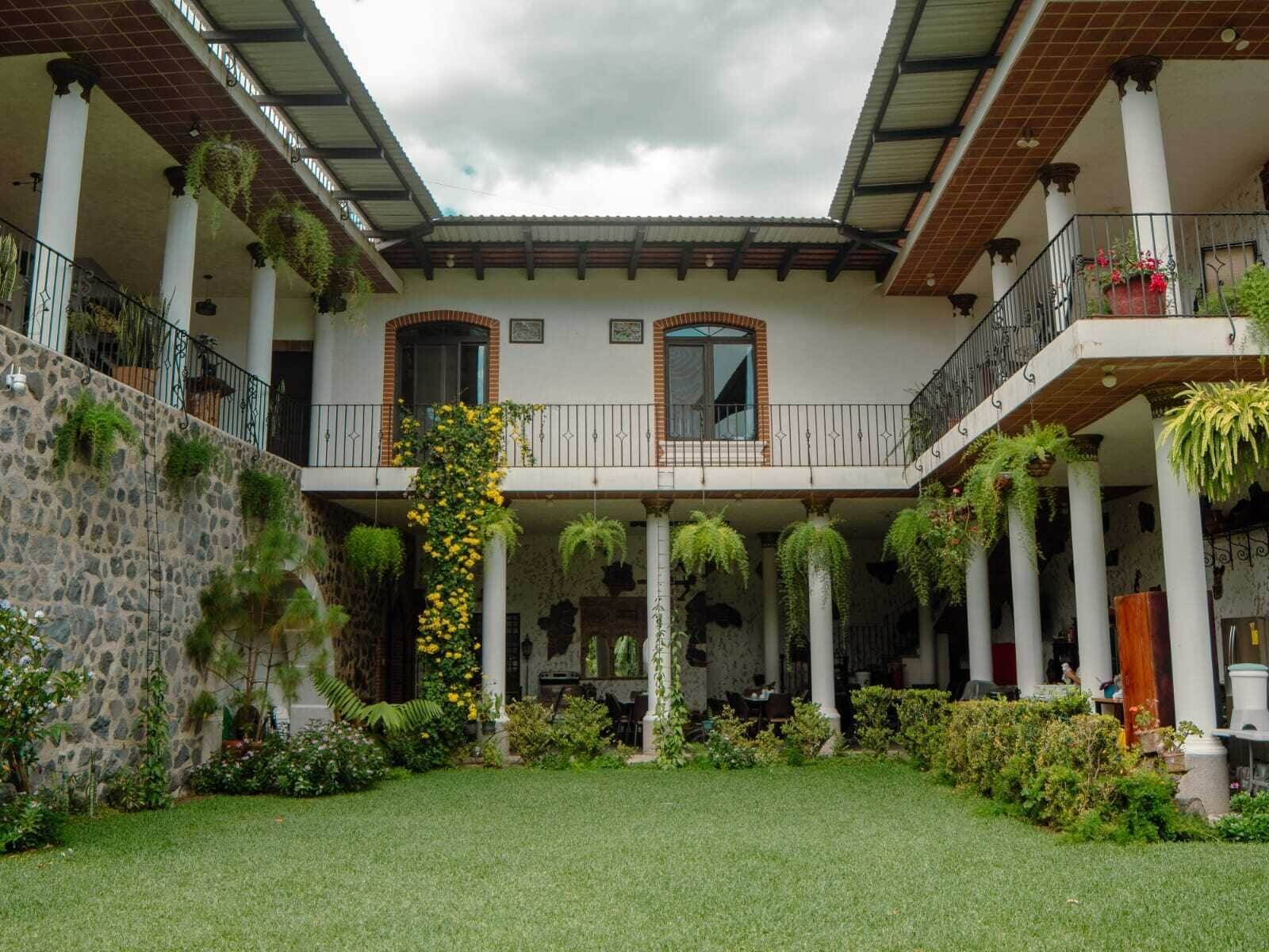 A courtyard with a central open space, surrounded by columns and covered balconies with hanging plants.