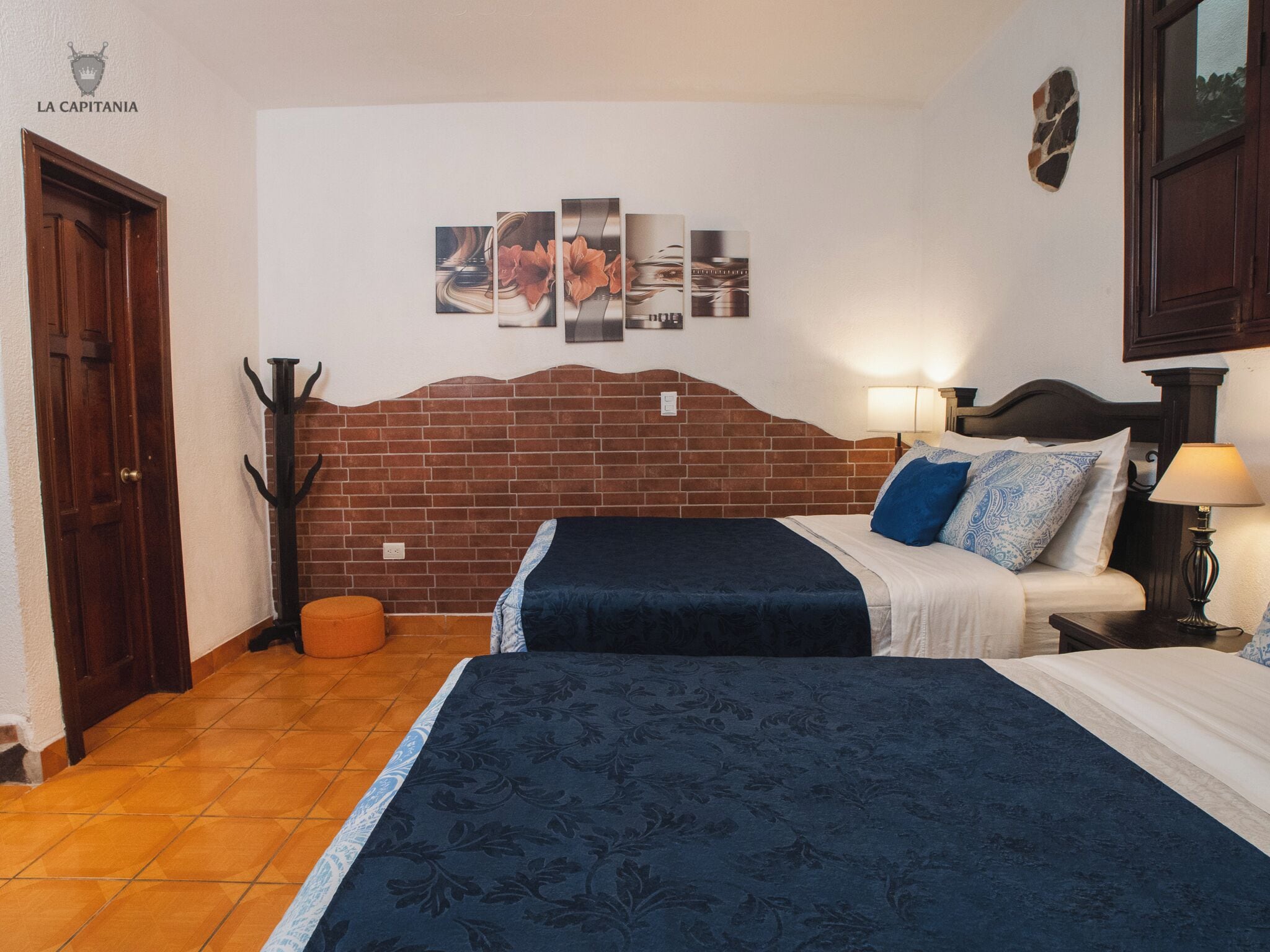 Ein Hotelzimmer mit Ziegelkopfteil, zwei Betten, einem Nachttisch mit Lampe, einem Wandbild und einem Kleiderhaken.