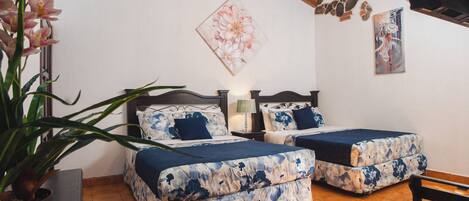 A bedroom with two beds, a potted plant, and a painting on the wall.
