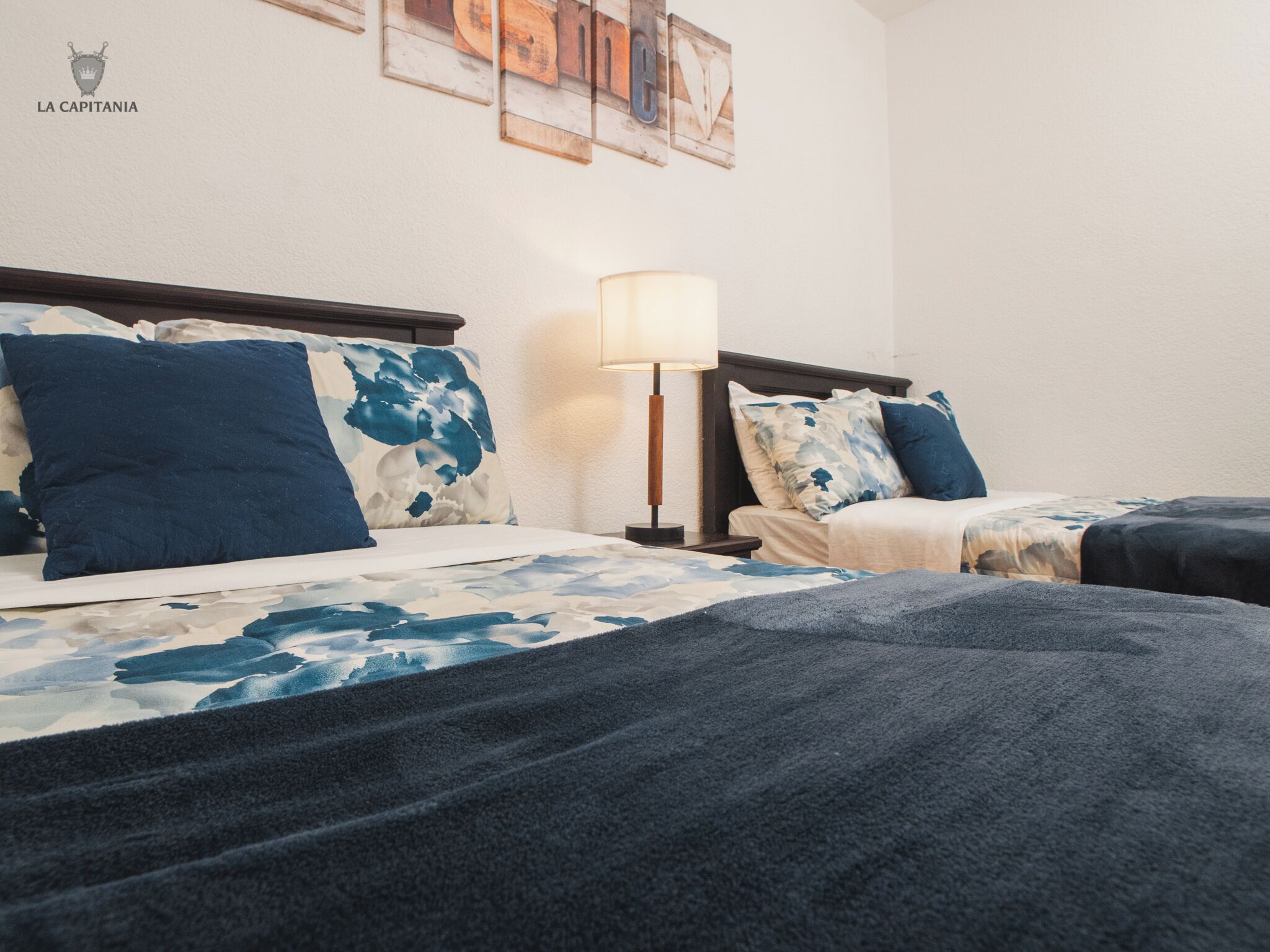Een hotelkamer met twee bedden, een nachtkastje met een lamp en een muur met kunst.