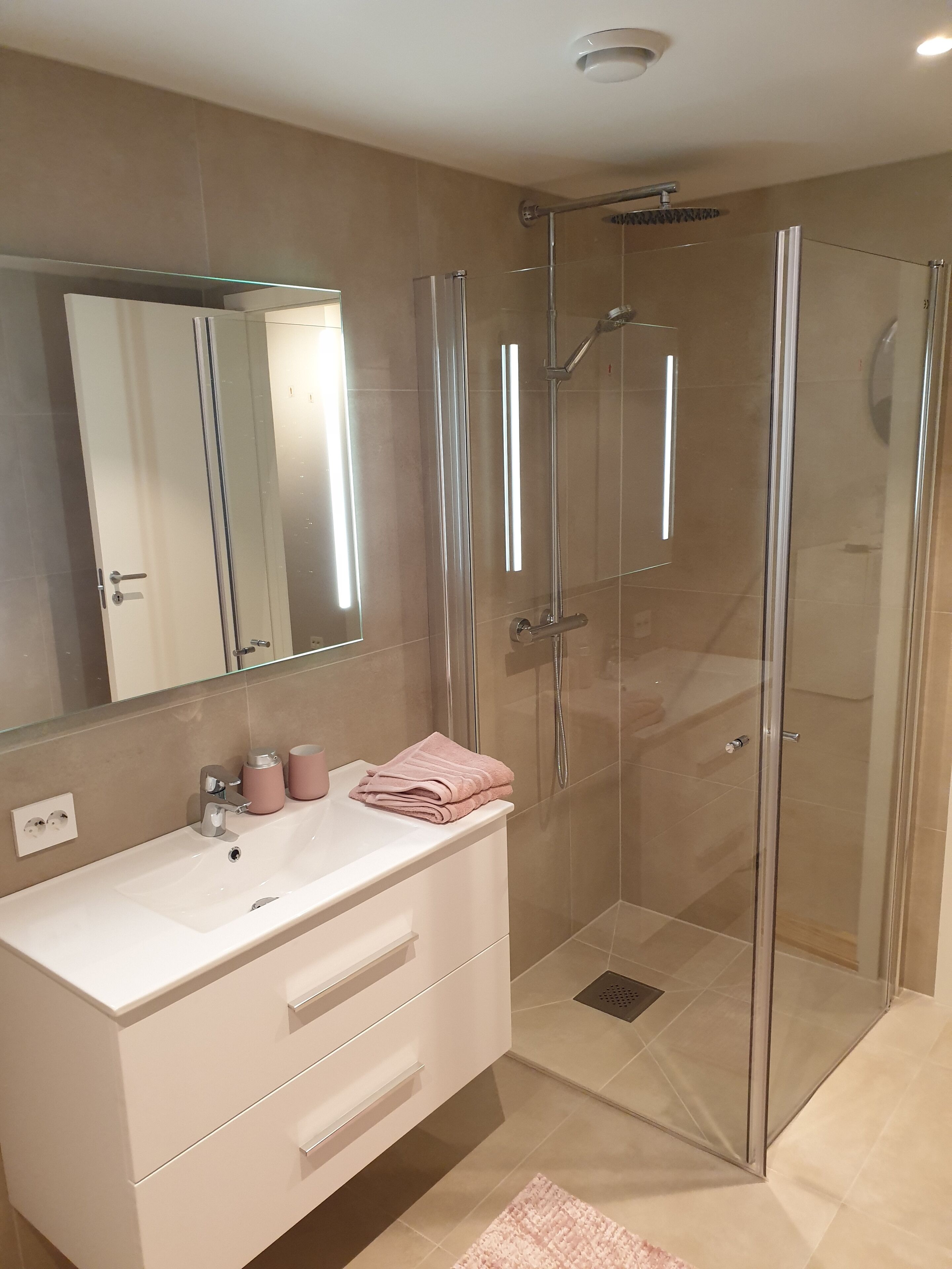 A modern bathroom with a glass-enclosed shower, a white vanity with drawers, and a large mirror.