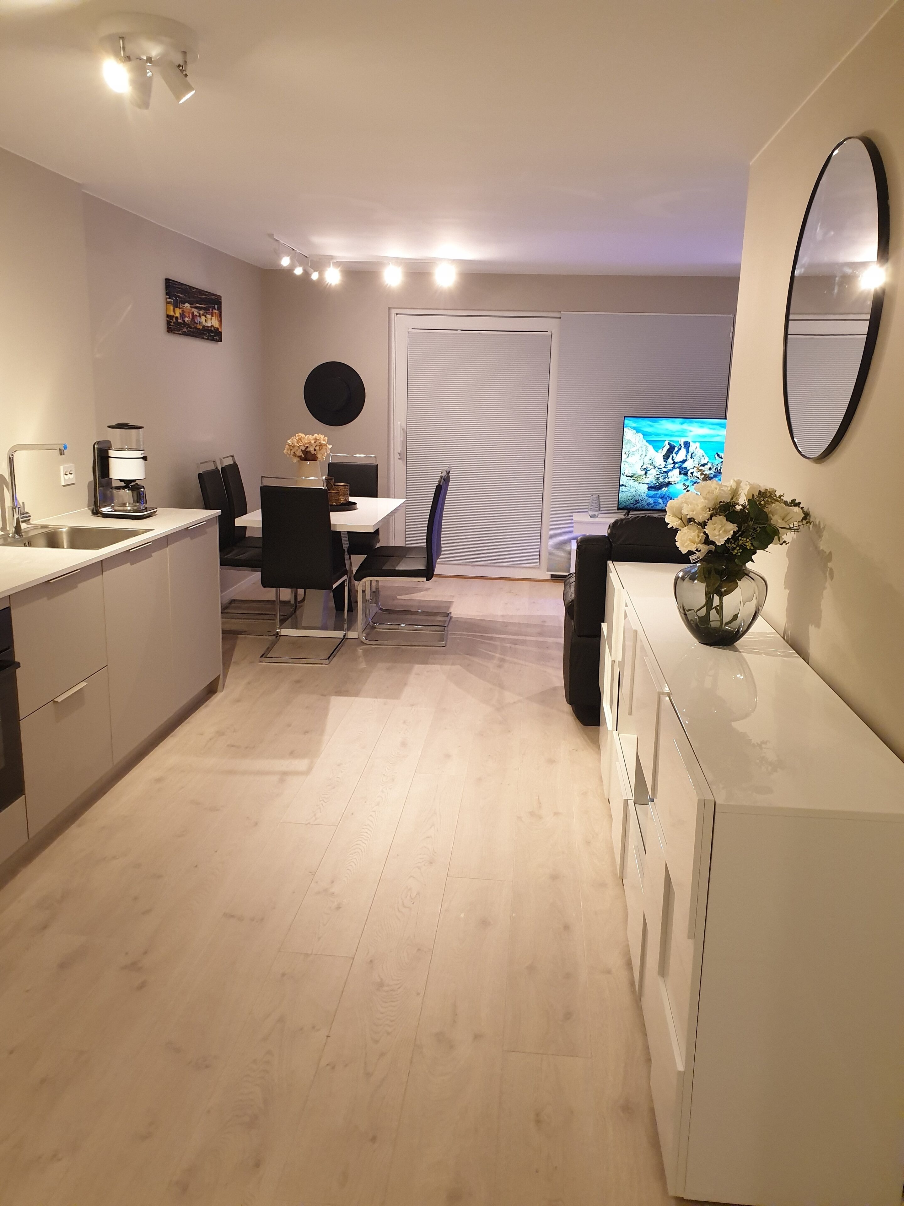 A modern kitchen with a dining area, a coffee machine, a TV, and a vase with flowers.