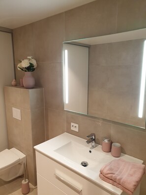 Un baño moderno con un lavamanos blanco, un espejo grande y azulejos color beige.