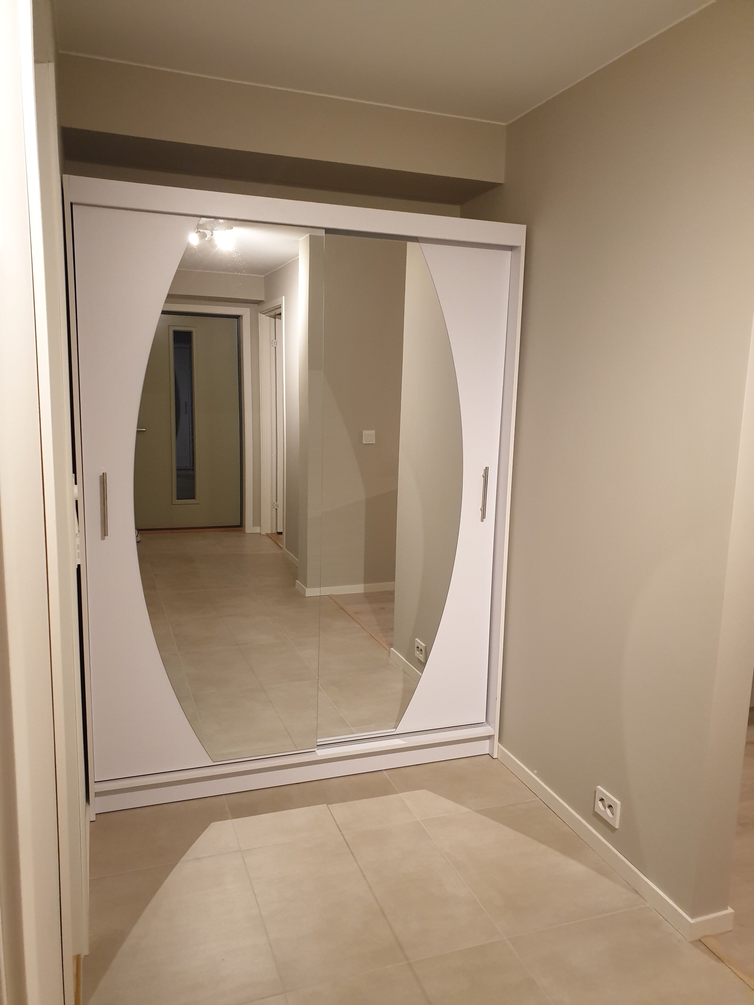 A room with a large mirror, beige walls, and a tiled floor.