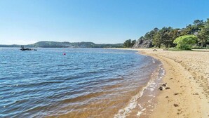 Una playa con agua azul cristalina, una orilla arenosa y un pequeño bote a lo lejos.