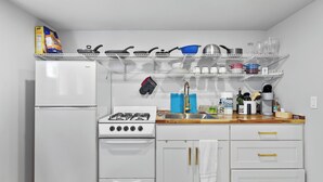 A compact kitchen with a white refrigerator, stove, and cabinets, featuring a wooden countertop and a shelf above holding various kitchen items. - Walk2UW, PrivateSuite w/Bath, FREE Parking,TV, WiFi (Seattle)