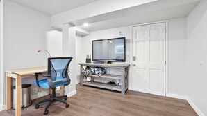 A small, well-lit room with a wooden desk, a blue office chair, a television on a stand, and a white door. - Walk2UW, PrivateSuite w/Bath, FREE Parking,TV, WiFi (Seattle)