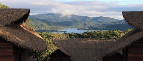 A thatched-roof structure with a view of a lake and mountains in the background.