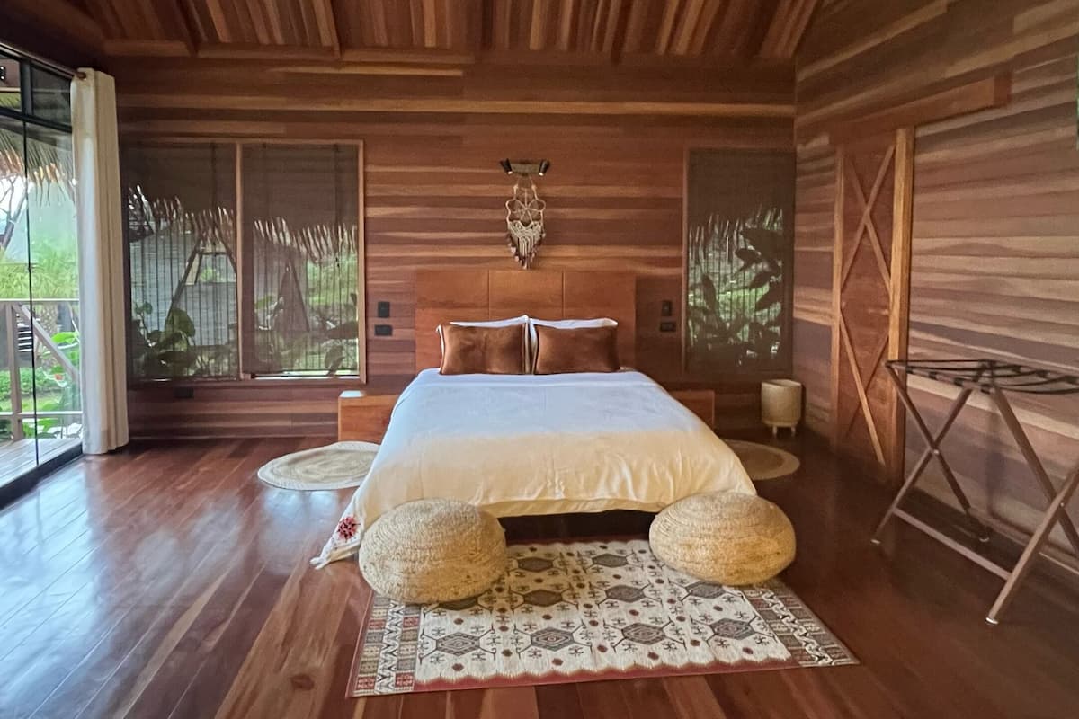 A spacious bedroom with a large bed, wooden flooring, and a high ceiling with skylight.