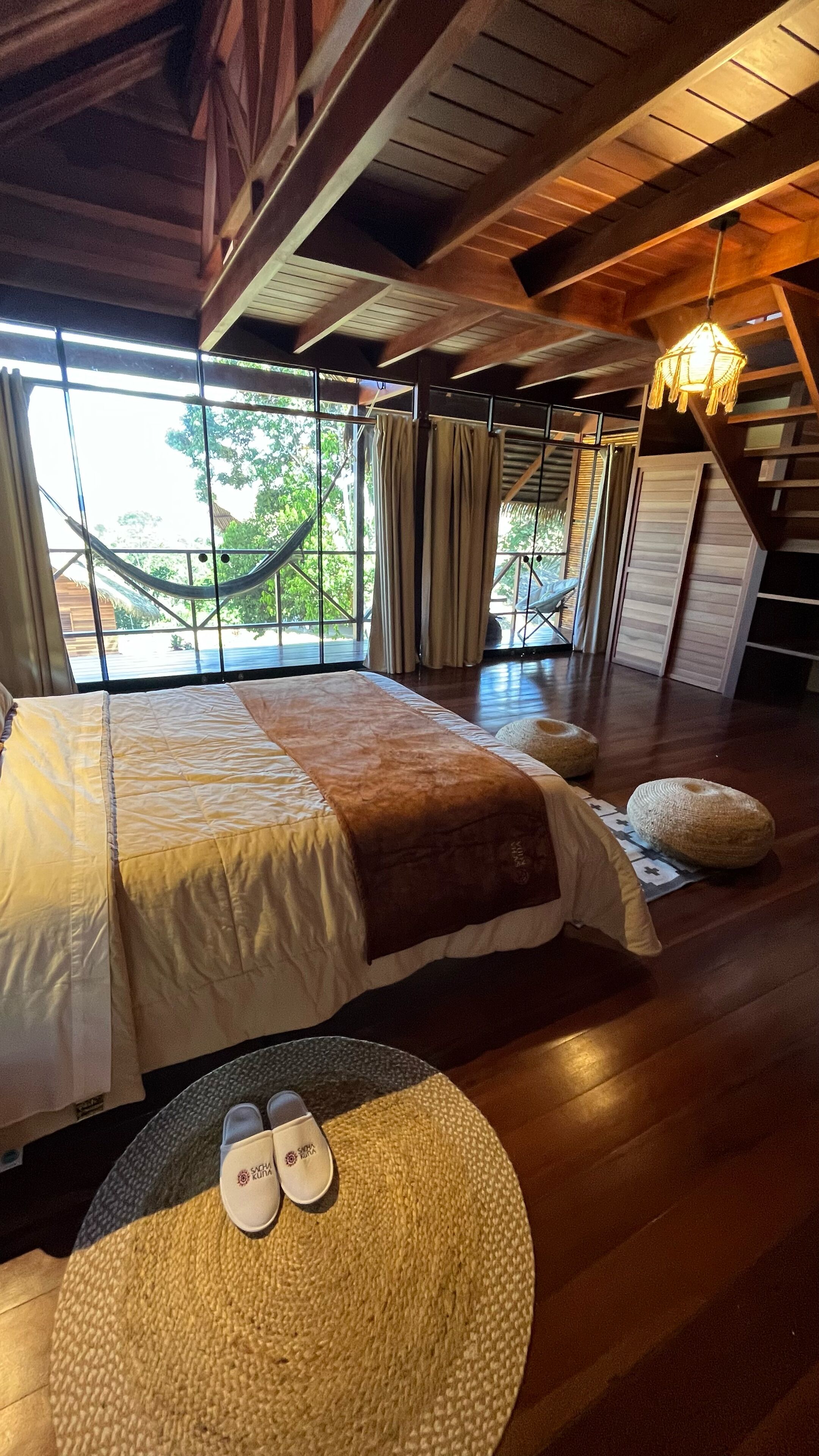 A spacious bedroom with a large bed, a view of the outdoors, and a hammock.