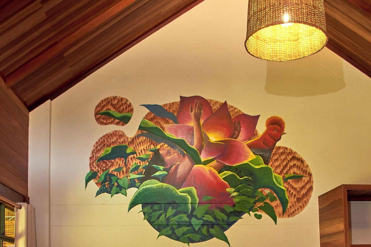 A living room with a large mural, a sofa, a TV stand, and a dining table with chairs.