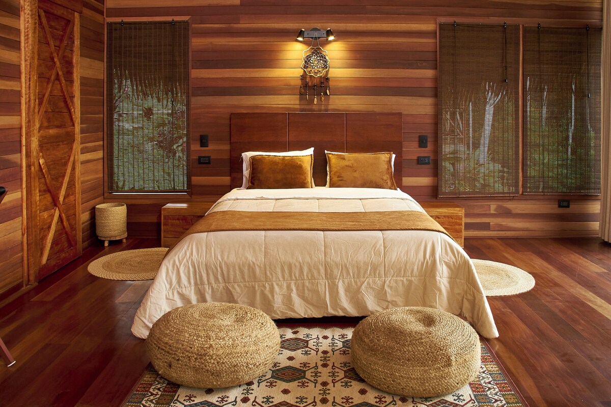A bedroom with a wooden headboard, a bed with white bedding, two bedside lamps, and a decorative wall hanging.