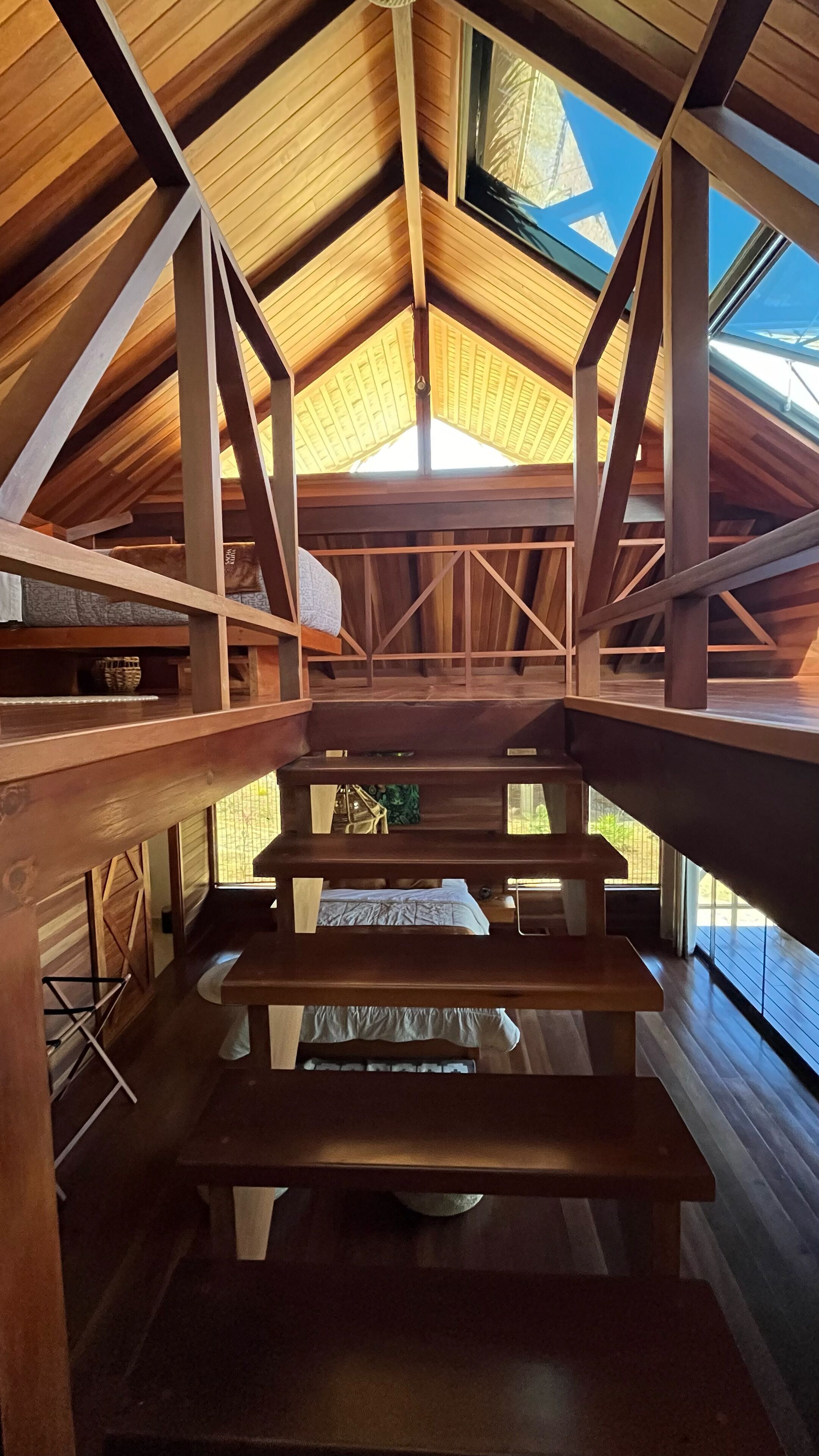 A wooden interior with a sloped ceiling and a skylight. There are wooden beams and a bench area.