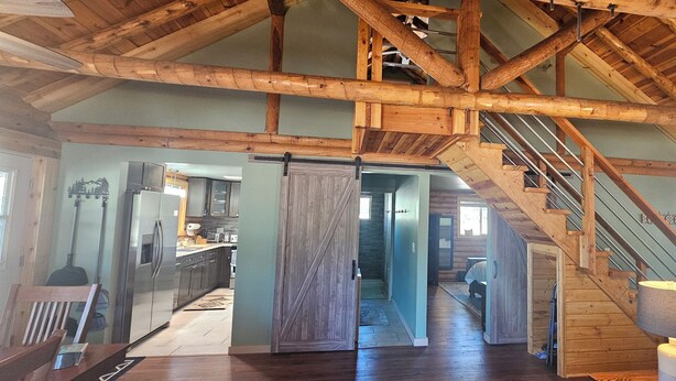 A spacious interior with a high ceiling, wooden beams, a kitchen area, and a staircase leading to an upper level. - Secluded luxurious 2‑bedroom cabin w/WiFi near Williams, AZ on 18 acres of pines (Williams)