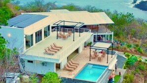 Una moderna casa a due piani con piscina sul tetto, ampie finestre e vista sull'oceano.