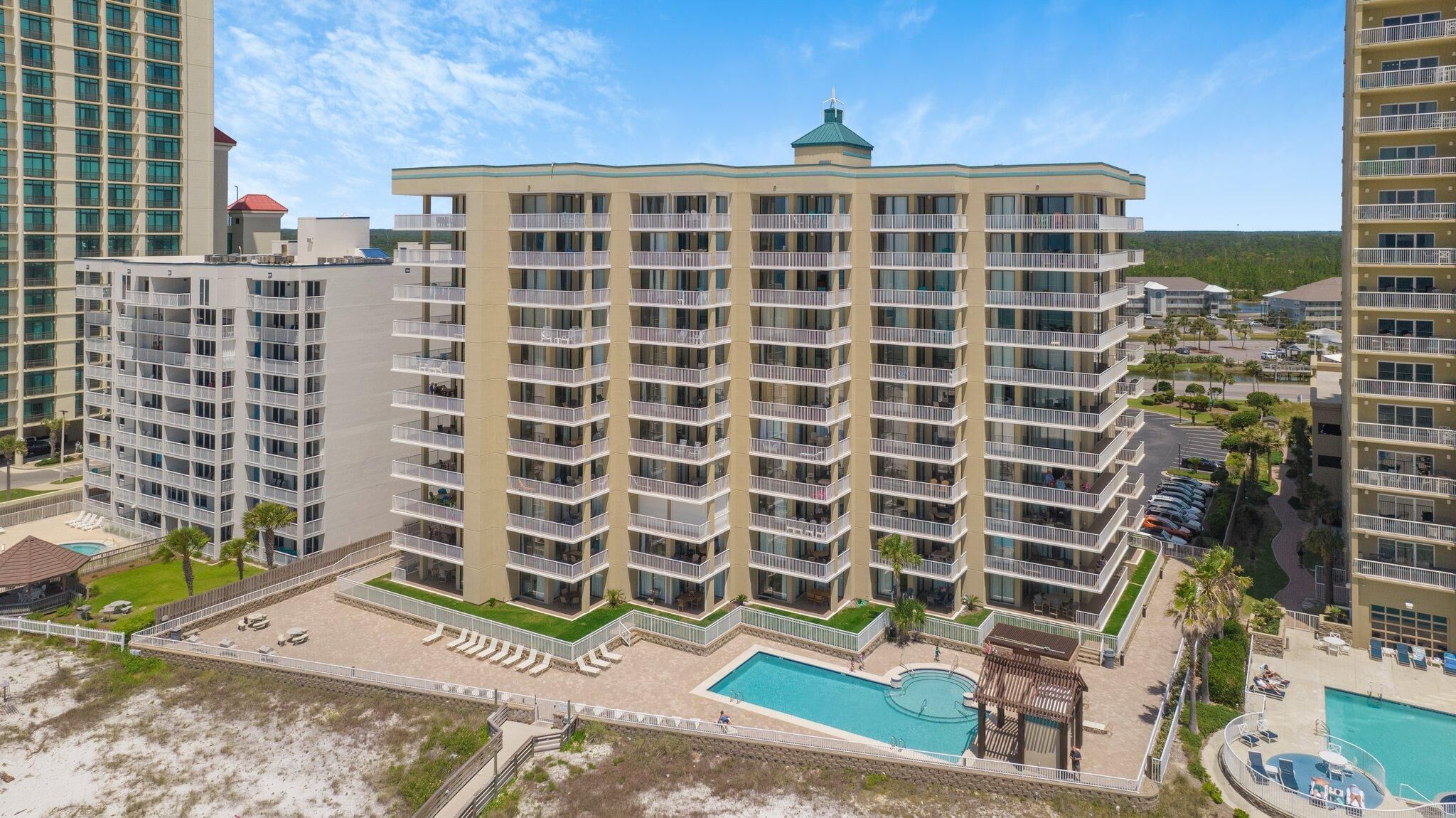 A high-rise hotel with multiple balconies, a swimming pool, and a landscaped area with lounge chairs.