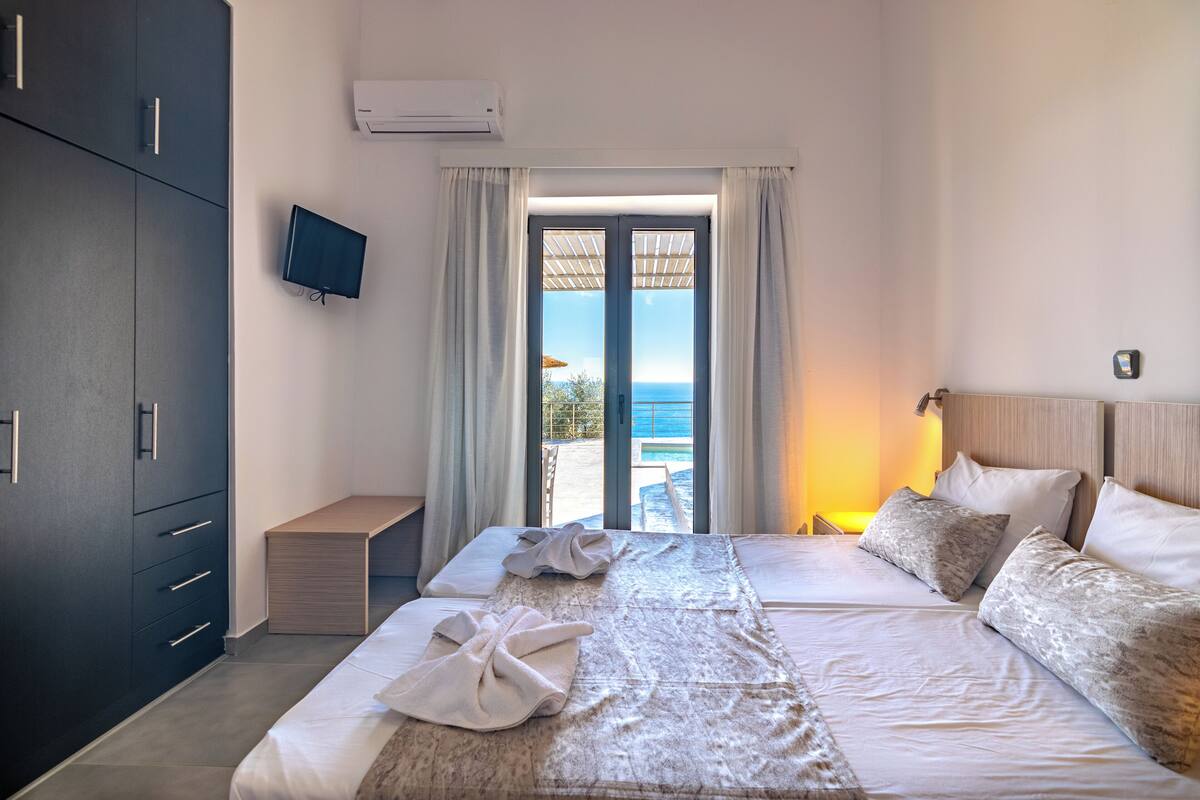Een hotelkamer met een bed, een televisie, een bureau en uitzicht op zee.