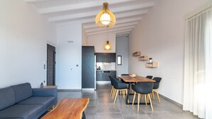 A modern living room with a sofa, a wooden coffee table, and a dining area with a table and chairs. - Pyrgos Plakias Villas (Agios Vasileios)