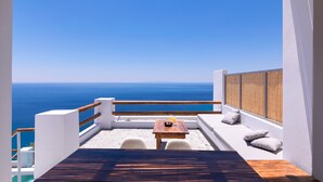 A balcony with a wooden table and chairs, a white cushioned bench, and a view of the sea. - Pyrgos Exclusive Villas (Agios Vasileios)