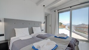 A modern bedroom with two beds, a large window with a view of the landscape, and a minimalist design. - Pyrgos Exclusive Villas (Agios Vasileios)