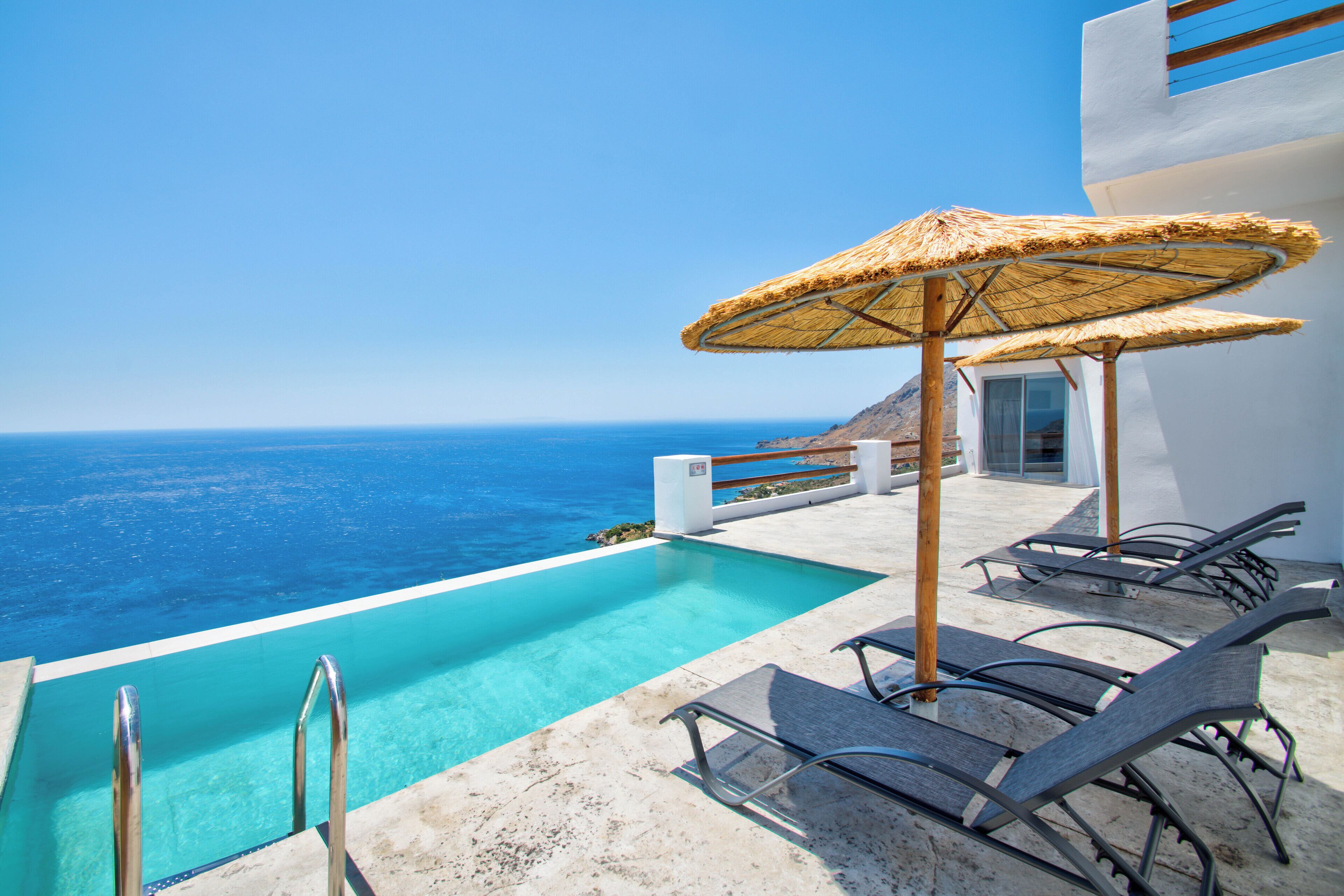 Ein Poolbereich mit freiem Blick auf den Ozean, Liegestühle und ein Reetdachschirm.