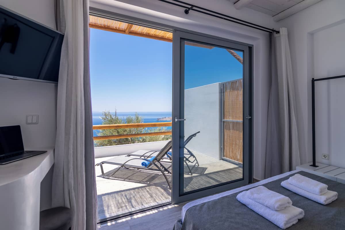 Une chambre avec un lit, une télévision et un balcon donnant sur la mer.