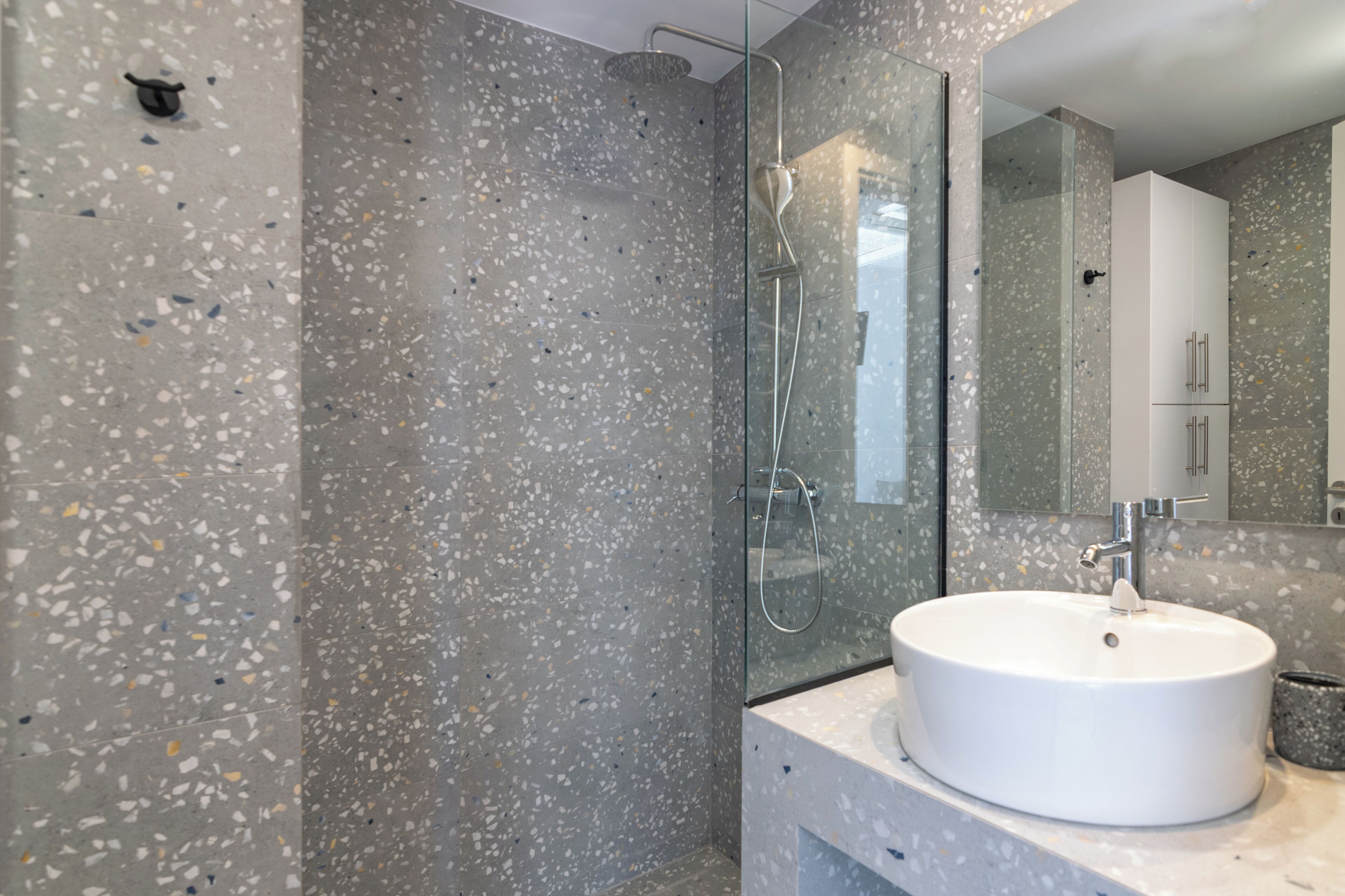 A modern bathroom with a glass-enclosed shower, a white sink, and a speckled tile backsplash.