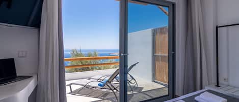 Une chambre avec un lit, une télévision, un balcon donnant sur la mer et un fauteuil.