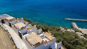 A coastal residential area with modern white buildings, a rocky island in the background, and a clear blue sea. - Pyrgos Exclusive Villas (Agios Vasileios)