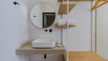 A modern bathroom with a white sink, round mirror, towel rack, and wooden shelves.