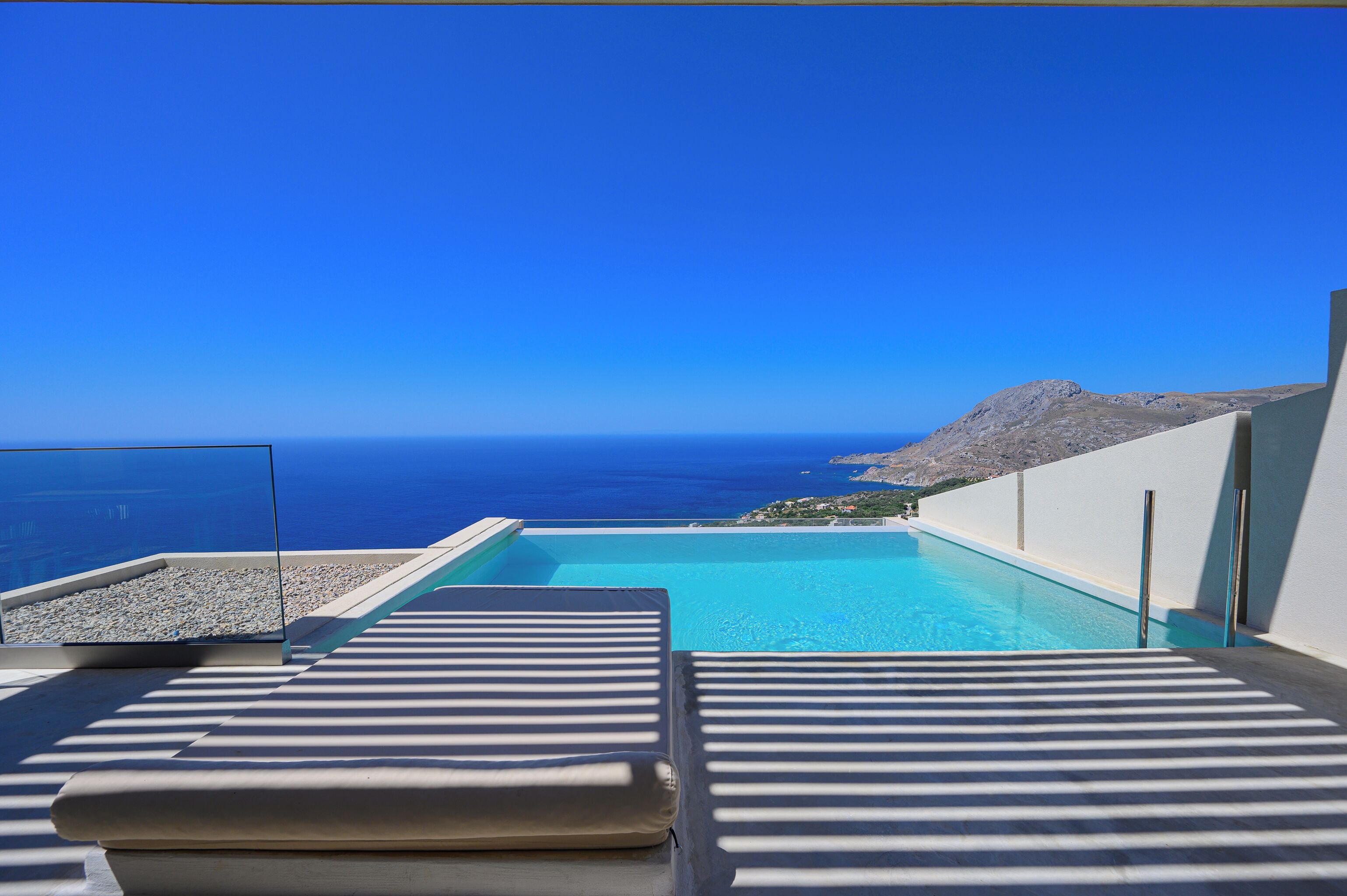 A poolside view with a clear blue sky and a distant view of the sea.