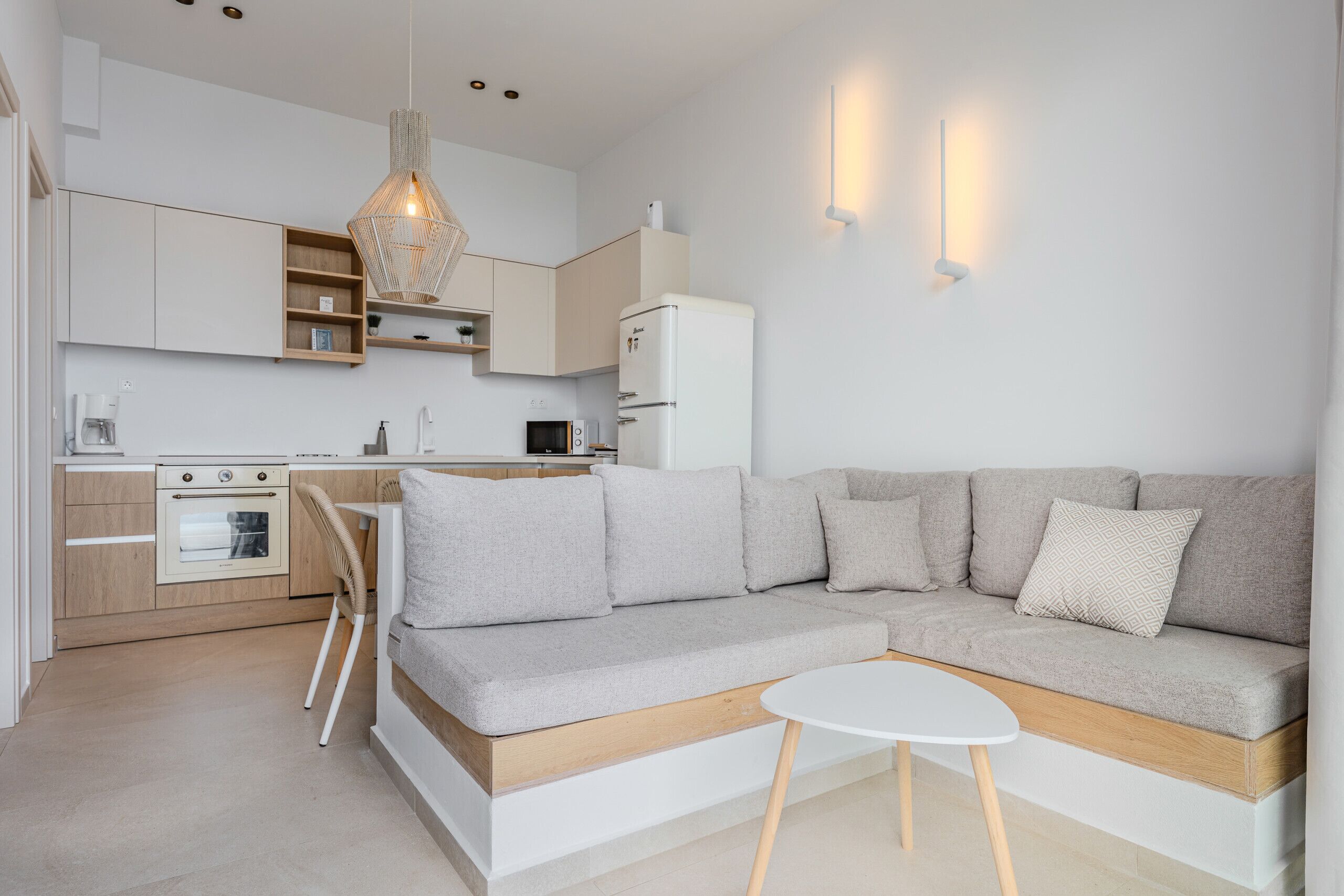 A modern kitchen with built-in appliances, a dining area with a white table, and a grey sofa.