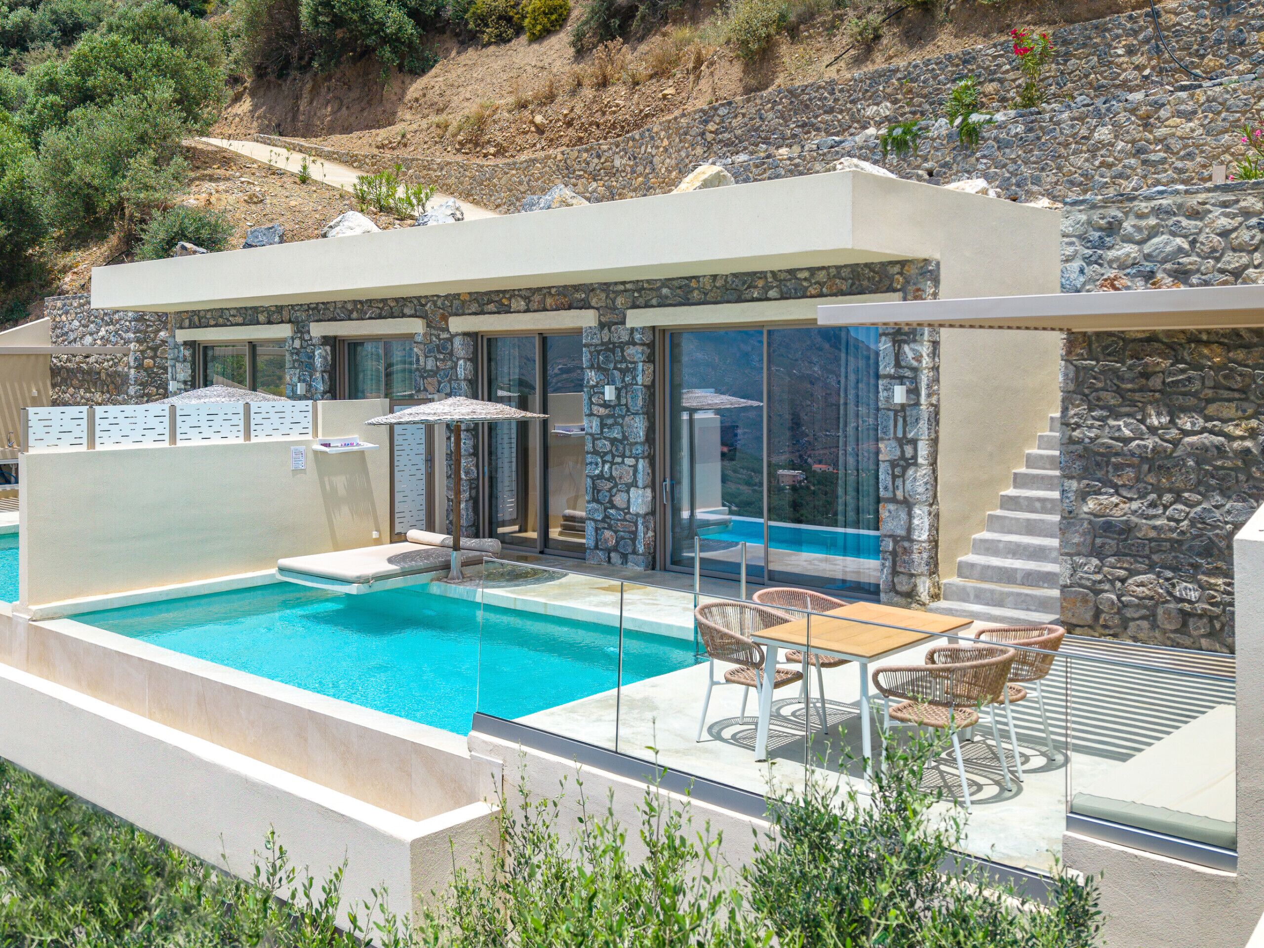 En modern villa med en swimmingpool, utomhusmöbler och väggar av sten.
