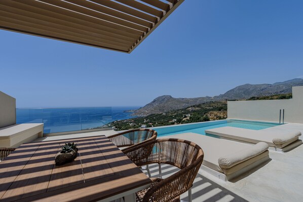 Una terraza con piscina, mobiliario de mimbre y vistas al mar y las montañas.