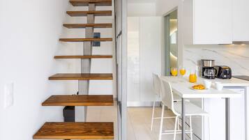 Una cocina moderna con armarios blancos, una mesa de comedor y una escalera con peldaños de madera.