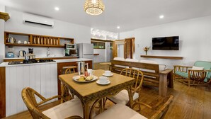 A modern kitchen with white cabinets, a dining area with wicker furniture, and a TV mounted on the wall. - Idle Awhile Beach - Family Suite in Negril (Negril)