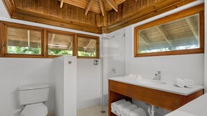 A bathroom with a wooden ceiling, a toilet, a shower, and a sink with a mirror. - Idle Awhile Beach - Family Suite in Negril (Negril)